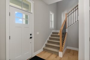 A white front door and small carpeted staircase with wooden handrail welcome you to 71 Elm Street’s bright entryway.