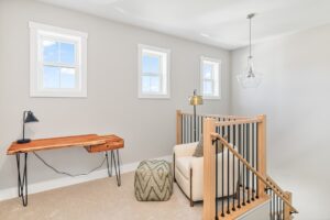 Small home office nook at 71 Elm Street with a wooden desk, lamp, pouf, and natural light from three windows.