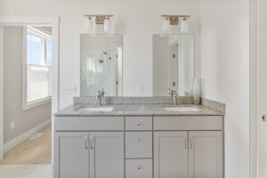 Modern bathroom at 71 Elm Street with double sinks, gray cabinets, granite countertop, and dual vanity mirrors.