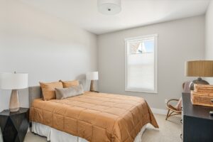 Bedroom at 71 Elm Street with a tan comforter, lamps on nightstands, a window, and a dresser with baskets.