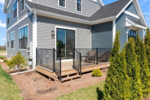 Small wooden deck with black railing at 71 Elm Street, overlooking a yard with shrubs and small trees.