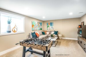 Bright basement game room at 68 Eden Lane with foosball table, couch, wall art, TV, and stylish accents.