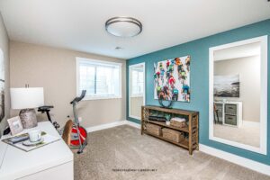 A bright exercise room at 68 Eden Lane with an exercise bike, console table, mirror, and colorful wall art.