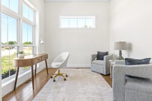 Bright home office at 385 Beaudry Lane with large windows, wooden desk, white chair, two gray armchairs, and a patterned rug.