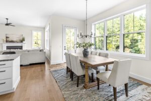 Bright dining area at 385 Beaudry Lane with a wooden table, six chairs, large windows, and a view into a cozy living room.