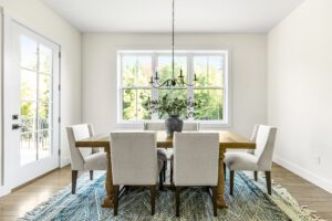 Bright dining room at 385 Beaudry Lane with a wooden table, six chairs, rug, and a window overlooking greenery.
