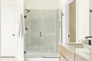 Modern bathroom at 385 Beaudry Lane features a glass shower, white towel on a hook, and wooden vanity with countertop.