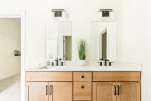 Modern bathroom at 385 Beaudry Lane with double sinks, wood vanity, black fixtures, and a plant between the sinks.