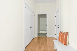 Hallway at 385 Beaudry Lane with light wood floor, white doors, and a bench with an orange pillow against a cream wall.