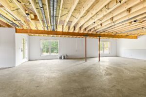 Unfinished basement at 385 Beaudry Lane with exposed beams, concrete floor, large windows, and white walls.