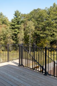 Wooden deck with black metal railing at 385 Beaudry Lane, overlooking trees and greenery on a sunny day.