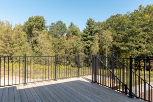 Wooden deck with black metal railing at 385 Beaudry Lane, overlooking green trees and a clear blue sky.