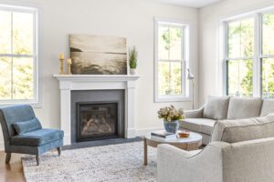 Bright living room at 385 Beaudry Lane with a fireplace, gray sofa, blue chair, and large windows filled with natural light.