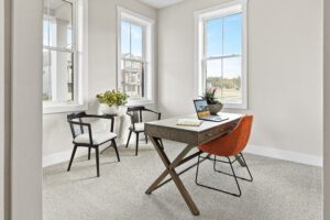 Bright home office at 68 Eden Lane with a desk, laptop, orange chair, two black chairs, and large windows.