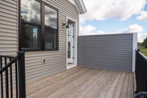 A small wooden deck at 68 Eden Lane features a gray privacy wall, black railing, and a door leading into the house.