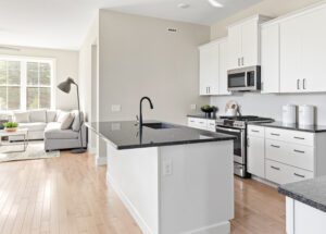 Modern white kitchen at 68 Eden Lane with black countertops, island sink, and stainless appliances; living area in background.
