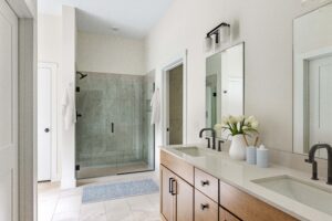Modern bathroom at 385 Beaudry Lane features double sinks, wood cabinets, glass shower, and fresh flowers on the counter.