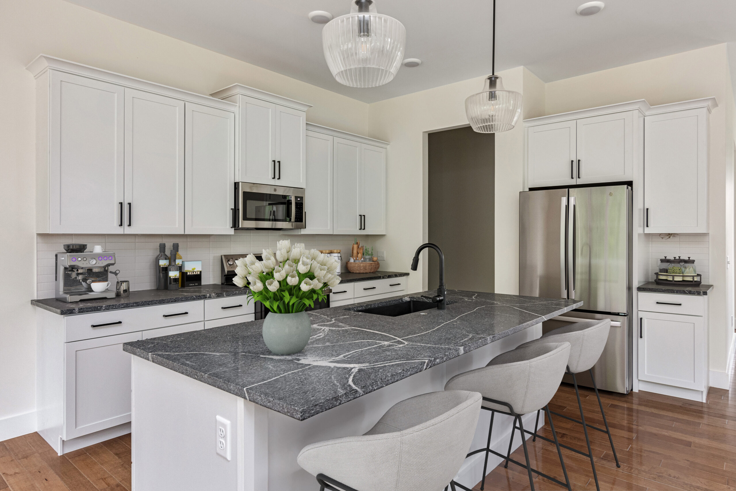 Modern kitchen at 385 Beaudry Lane with white cabinets, black marble island, bar stools, and tulips on the counter.