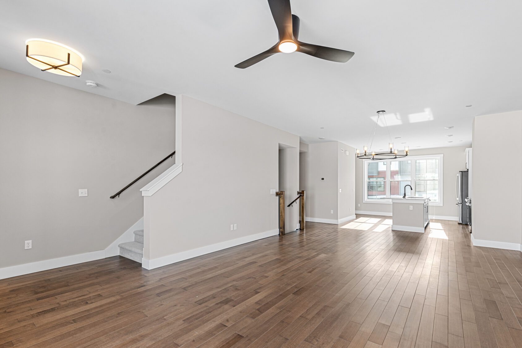 Modern open-concept living space at 188 Alpine Drive with wood floors, ceiling fan, stairway, and kitchen in the background.