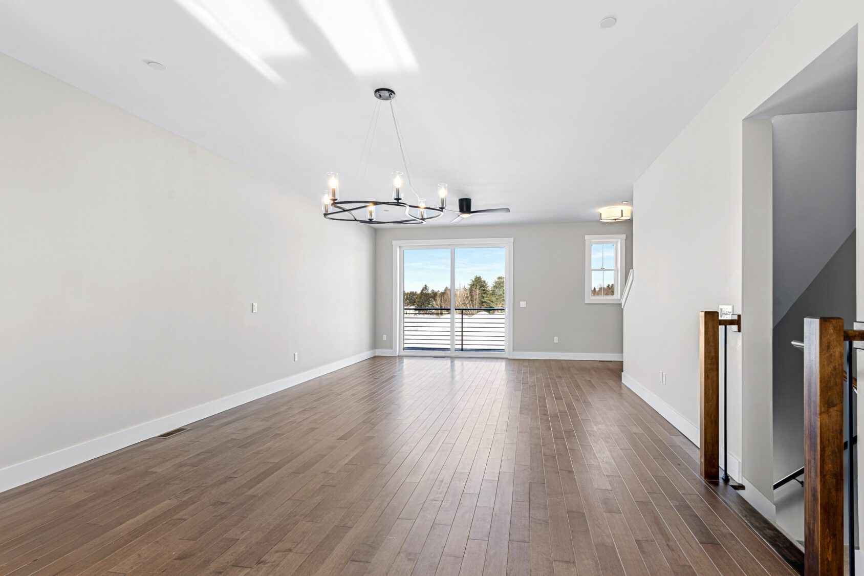 Bright empty room at 188 Alpine Drive with wood floors, modern chandelier, large window, and balcony access.