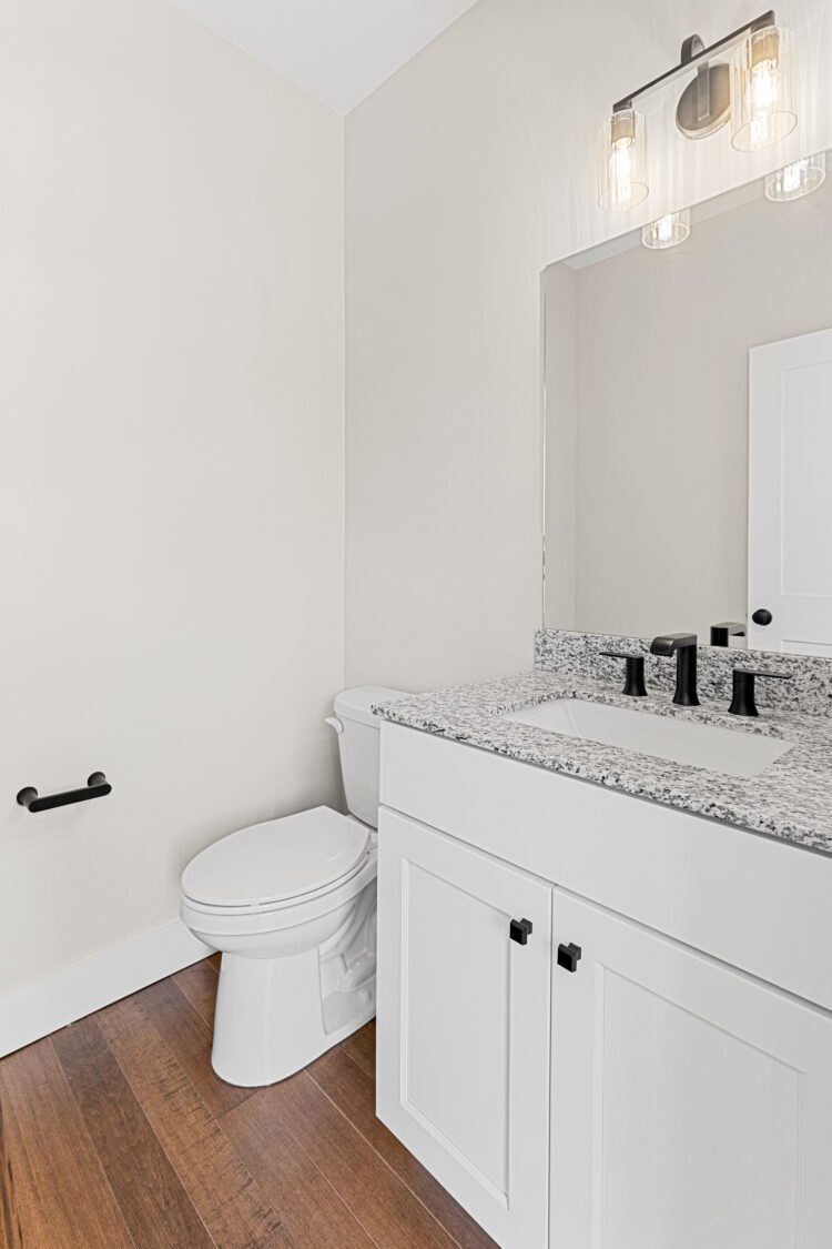 Modern bathroom at 188 Alpine Drive with white vanity, granite countertop, black fixtures, toilet, and wood flooring.