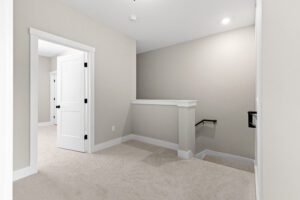 Carpeted hallway at 188 Alpine Drive with beige walls, white trim, a room door, and stairs with a black handrail.