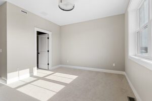 Empty beige bedroom at 188 Alpine Drive with carpet, white trim, open door, large window, and ceiling light fixture.