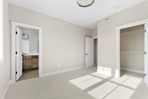 Empty bedroom at 188 Alpine Drive with beige walls, open closet, bathroom entrance, and sunlight streaming through windows.