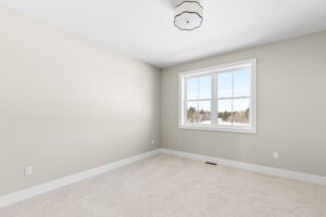 Empty beige room with carpeted floor, white trim, large window, and ceiling light fixture at 188 Alpine Drive.