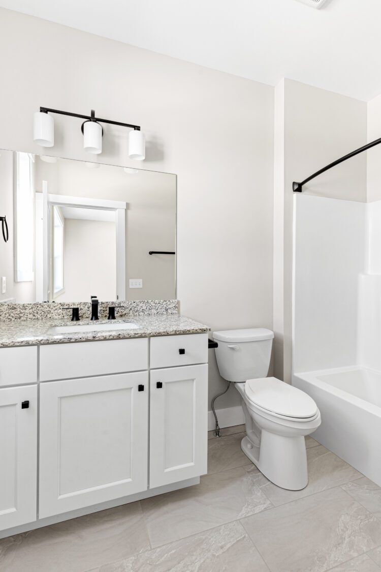 Modern bathroom at 188 Alpine Drive with white cabinets, a toilet, large mirror, and a bathtub with shower curtain rod.