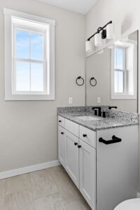 Modern bathroom at 188 Alpine Drive with granite countertop, white cabinets, large mirror, window, and black fixtures.