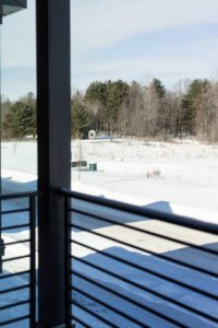 A snowy landscape with trees in the background, viewed from behind a balcony at 188 Alpine Drive.