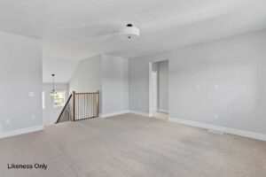 Spacious empty room at 136 Elm Street with light gray walls, beige carpet, and a ceiling light near a staircase railing.