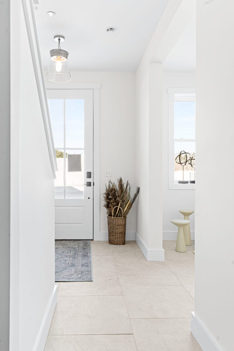 Bright entryway at 196 Alpine Drive with a white door, dried plants in a basket, and a side table on light tile flooring.