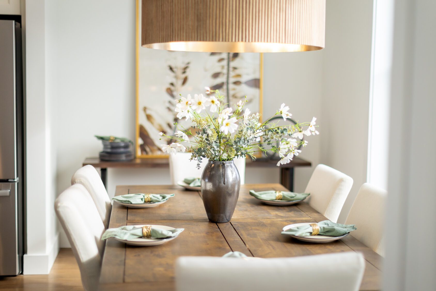 A dining table set for four at 196 Alpine Drive, with white flowers and a large pendant light overhead.