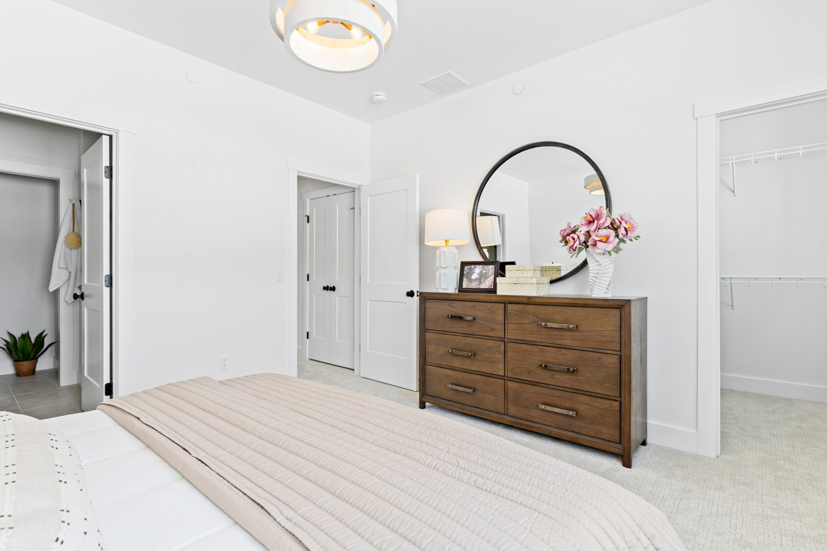A modern bedroom at 196 Alpine Drive features a wooden dresser, round mirror, flowers, and neutral decor.