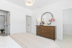 A modern bedroom at 196 Alpine Drive features a wooden dresser, round mirror, flowers, and neutral decor.