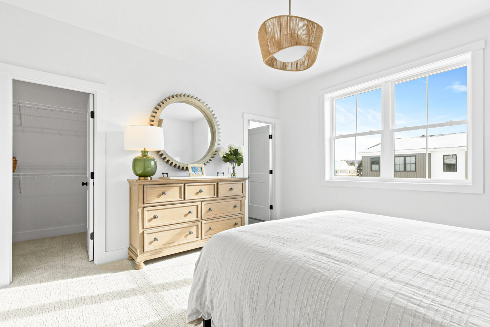 Bright bedroom at 196 Alpine Drive with white walls, a large bed, wooden dresser, round mirror, and natural light.