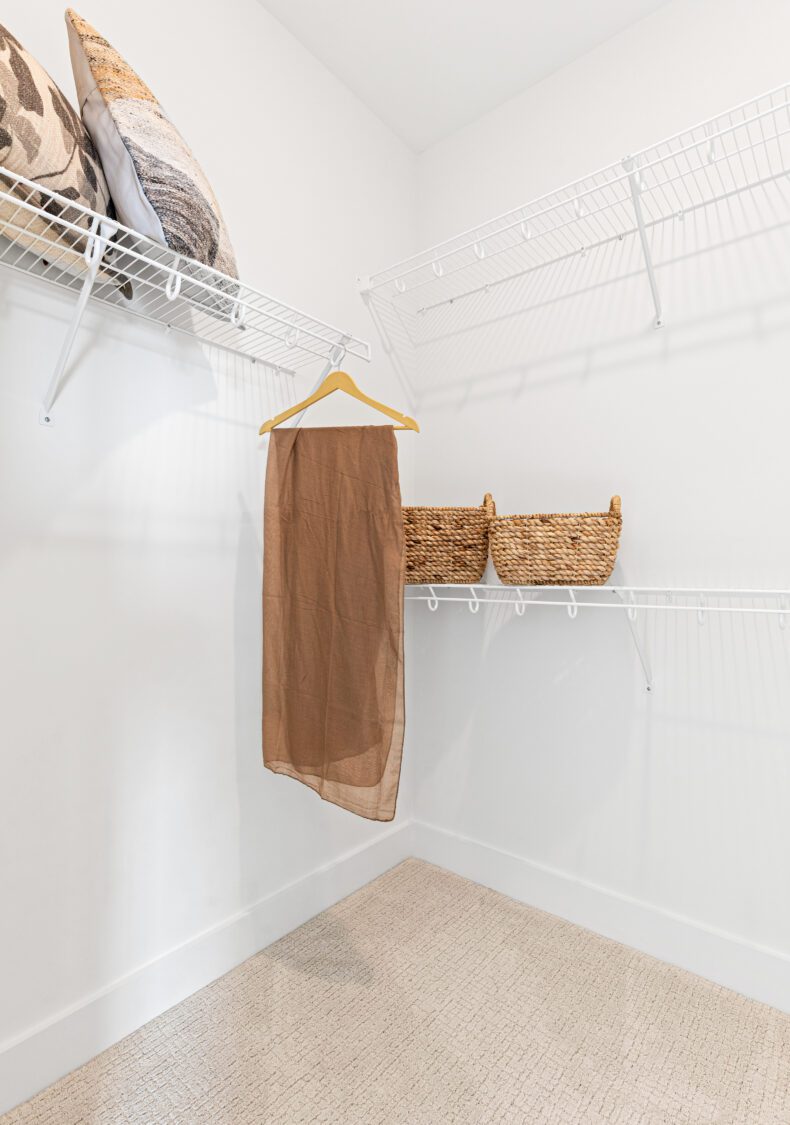 Minimalist walk-in closet at 196 Alpine Drive with wire shelves, baskets, pillows, and a brown scarf on a yellow hanger.