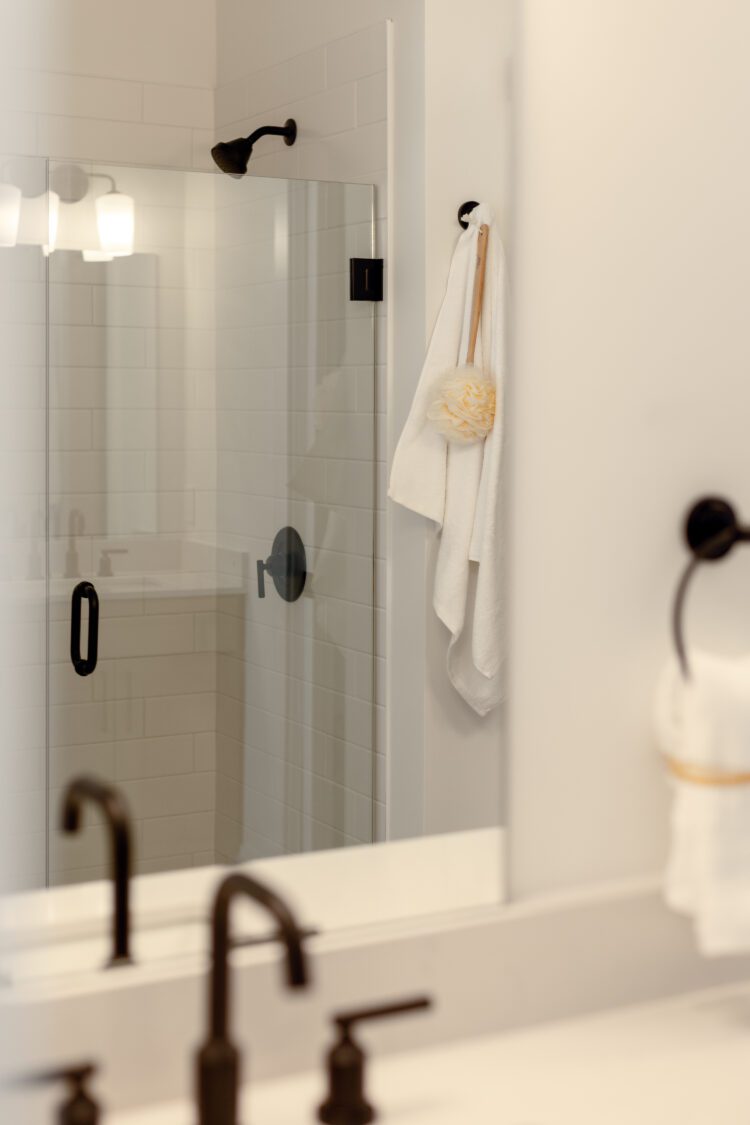 Modern bathroom at 196 Alpine Drive with glass shower, white towel, bath sponge on wall hook, and sleek black fixtures.