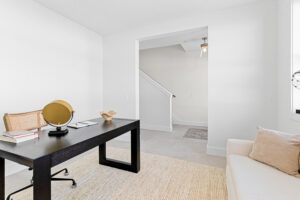 Minimalist home office at 196 Alpine Drive with black desk, books, a chair, and beige sofa on a light rug.