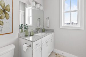 Modern bathroom at 196 Alpine Drive with white cabinets, granite countertop, mirror, window, and green decor accents.