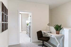 Small home office at 162 Alpine Drive with a white desk, dark chair, plant, and wall art by an open doorway to the bedroom.