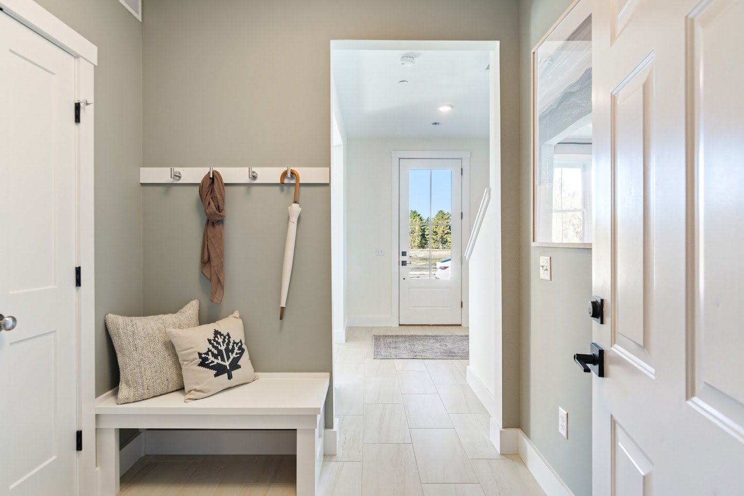 A bright entryway at 162 Alpine Drive with a bench, pillows, coat rack, scarf, umbrella, and a door leading outside.
