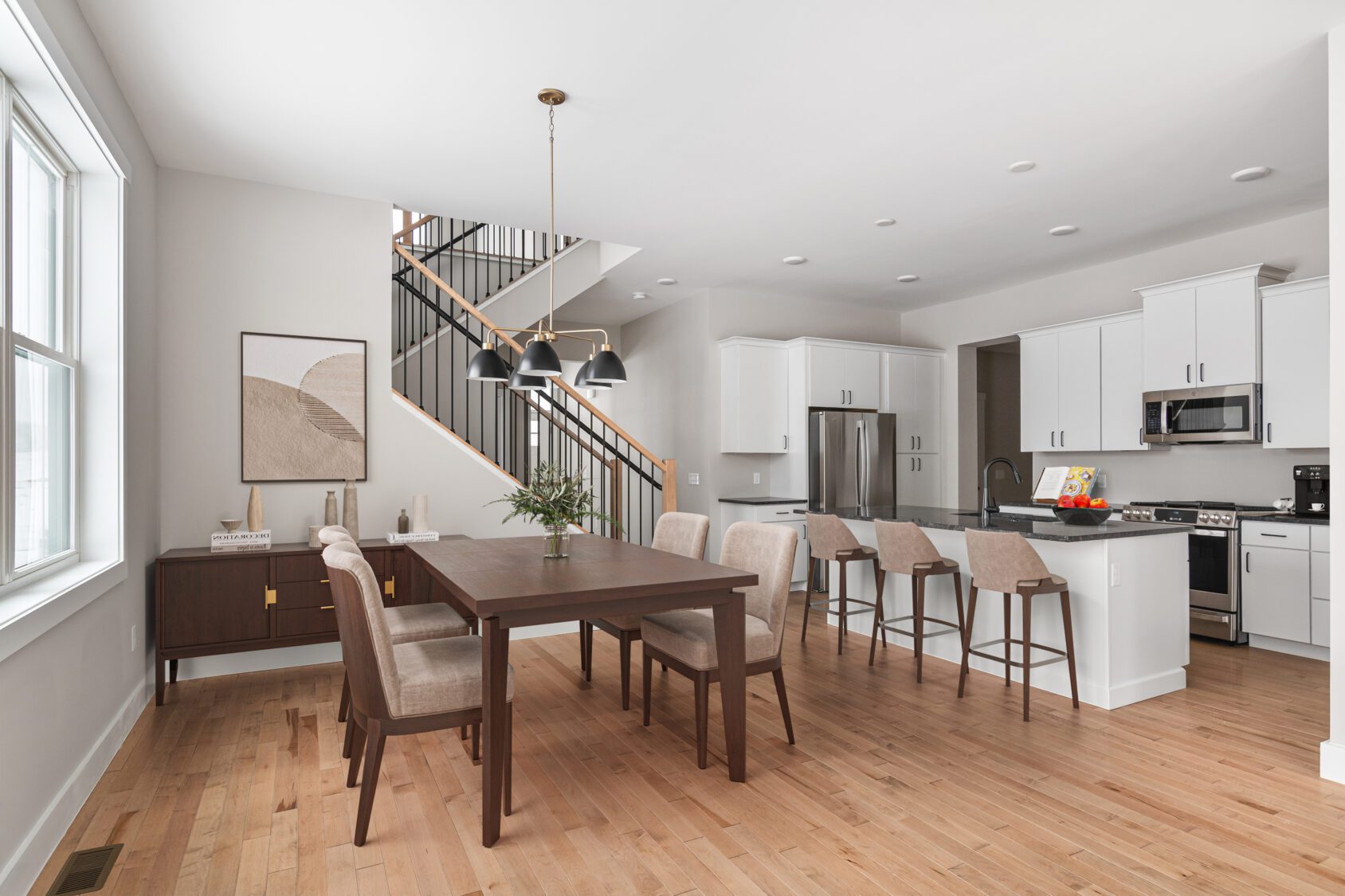 Modern Castlerock kitchen and dining area with wood floors, white cabinets, and dark wood table in Paired Villa style.