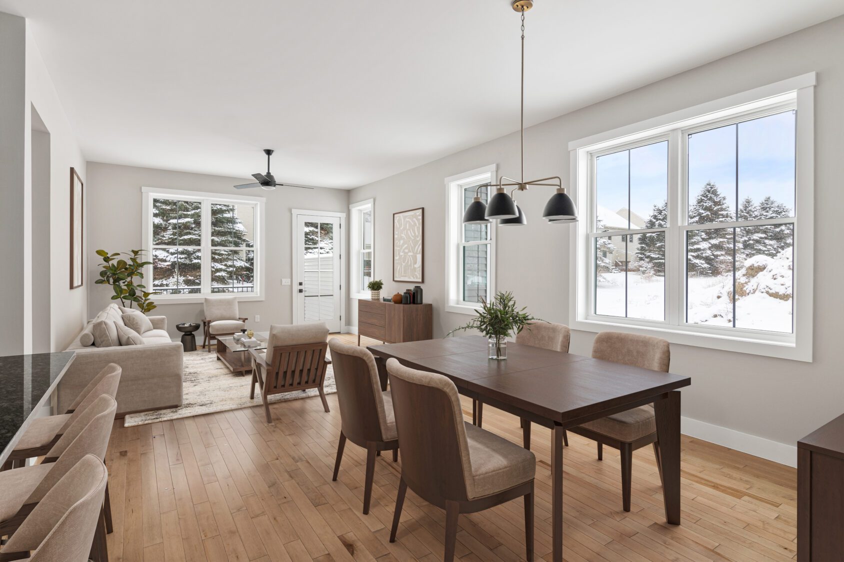 Bright dining and living area in a Castlerock Paired Villa with wooden furniture and snowy views through large windows.