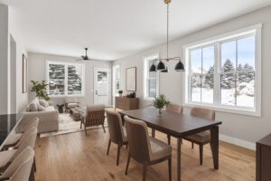 Bright dining and living area in a Castlerock Paired Villa with wooden furniture and snowy views through large windows.