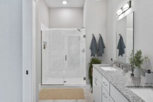 Modern Castlerock bathroom with glass shower, granite countertop, double sinks, and two blue towels in a Paired Villa.